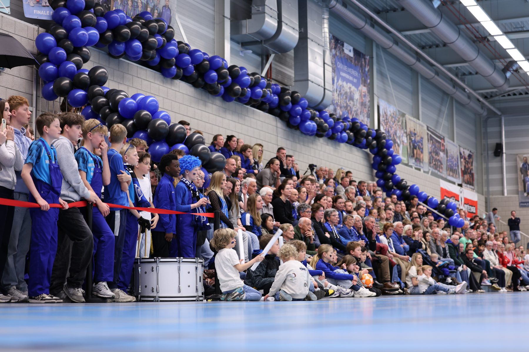 Volle sporthal van CKV Nieuwerkerk met blauw-zwarte ballonbogen, drummers en publiek tijdens een recente wedstrijd